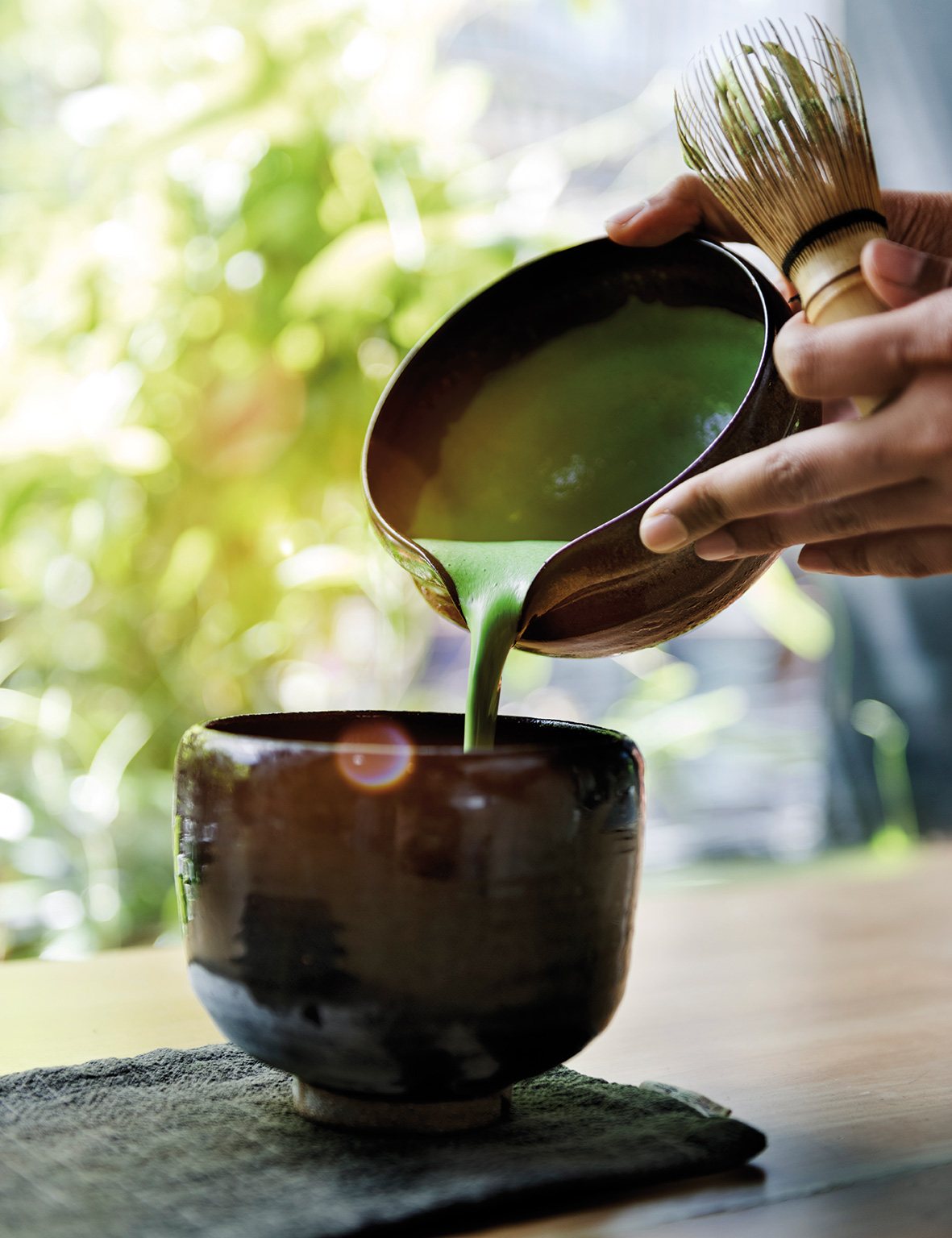 Matcha being poured from a chawan into a bowl with a bamboo whisk